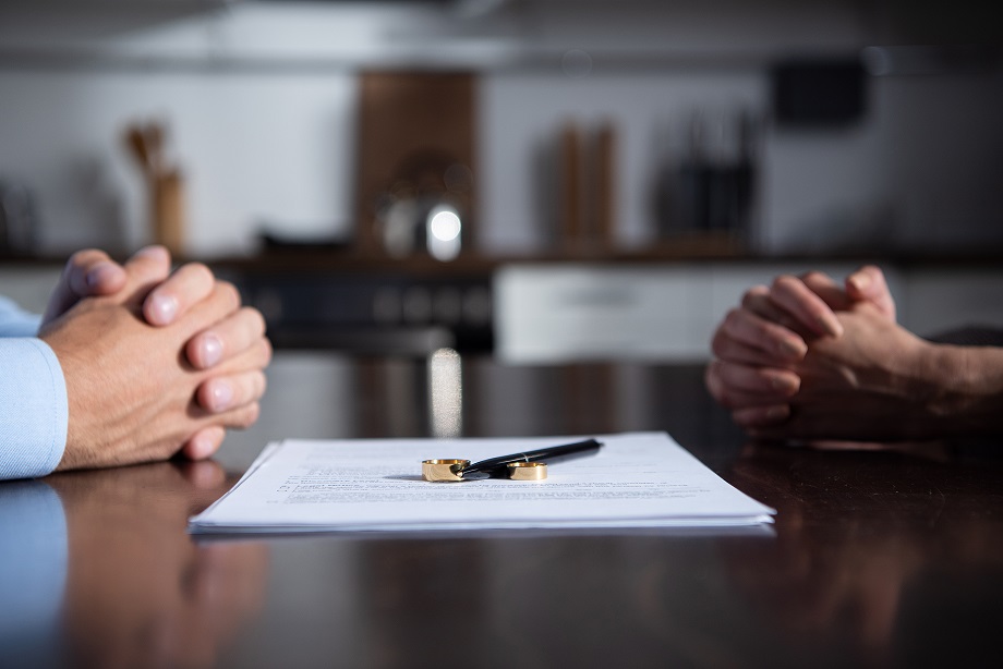 partial view of couple sitting at table with clenched hands near divorce documents